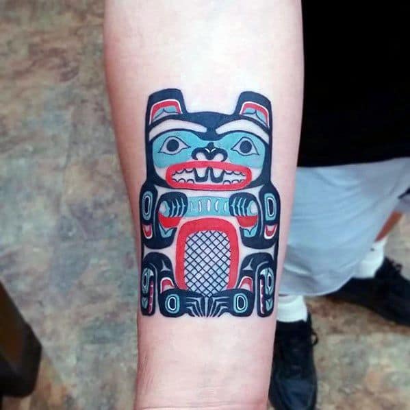 Forearm beaver tattoo in bold Indigenous art style, featuring red, black, and blue patterns with symmetrical and symbolic detailing.