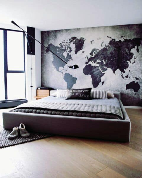 Minimalist bedroom with a world map mural, grey bed, and large window featuring a lamp and shoes on the floor