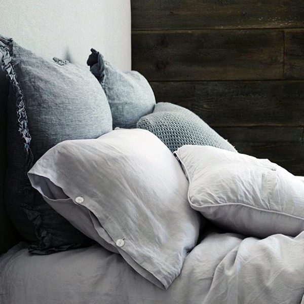 A bed with grey and white pillows against a dark wooden wall