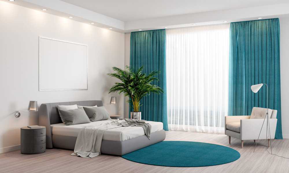 Modern bedroom with teal curtains, grey bed, indoor plant, and round blue rug.