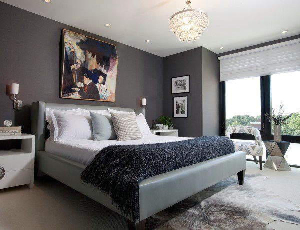 Modern bedroom with a grey accent wall, stylish bed, chandelier, abstract art, and large window with a view