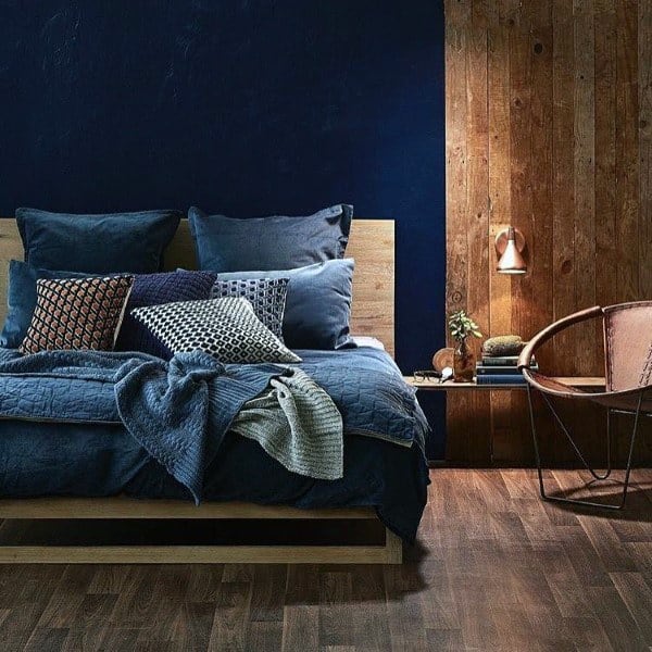 Modern bedroom with a navy blue accent wall, wooden elements, and cozy layered bedding with patterned cushions.