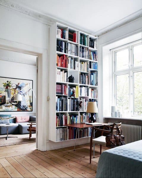 Cozy room with a towering bookshelf, desk, chair, and large window lighting the space