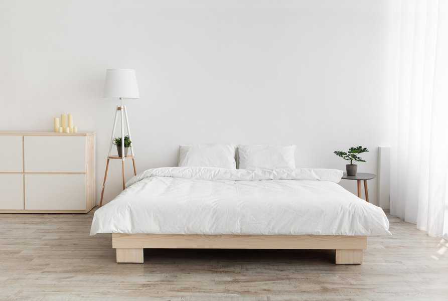 Minimalist white bedroom with platform bed, floor lamp, and light wood furniture.