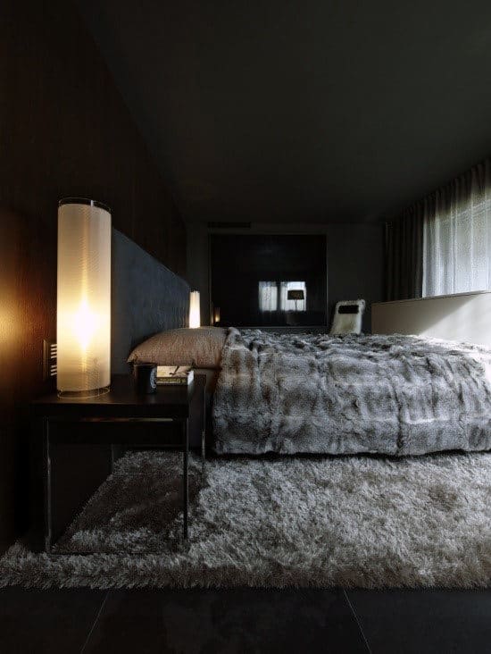 A modern bedroom with a gray rug, bedside lamps, and a fur blanket on the bed