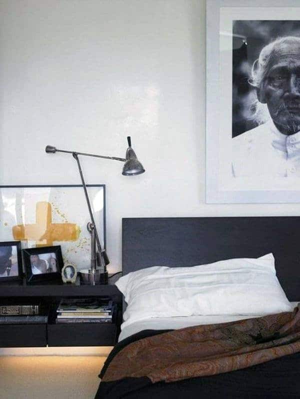 A modern bedroom with wall art, a black bed, and a lamp on a bedside table.