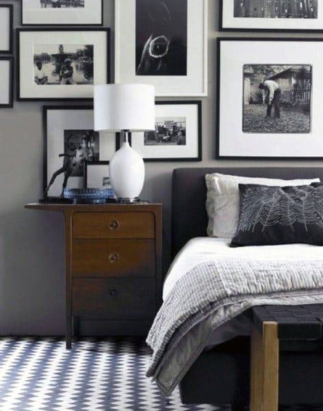 A bedroom featuring a grey bedside table, a lamp, and black-and-white framed photos on the wall above the bed