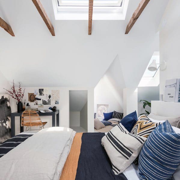 Cozy attic bedroom with skylight, exposed beams, patterned pillows on a comfy bed, and a corner desk
