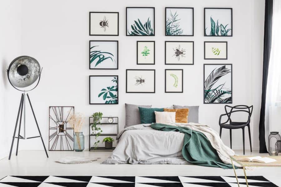 Bedroom with framed botanical wall art, tripod lamp, and modern black chair.
