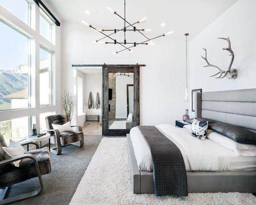 Rustic bedroom with platform bed, deer skull wall art, and large windows.