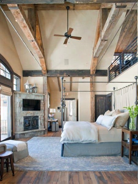 Spacious rustic bedroom with high ceiling, four-poster bed, and stone fireplace.