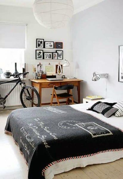 Bedroom with a bicycle, desk, and black bedspread; wall art and study lamp add decor