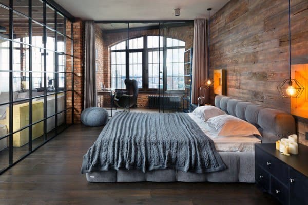 Industrial bedroom with glass partition, wooden accent wall, and cozy gray bedding.