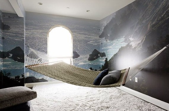 Indoor hammock in a bedroom with ocean-themed wallpaper and soft carpet flooring.