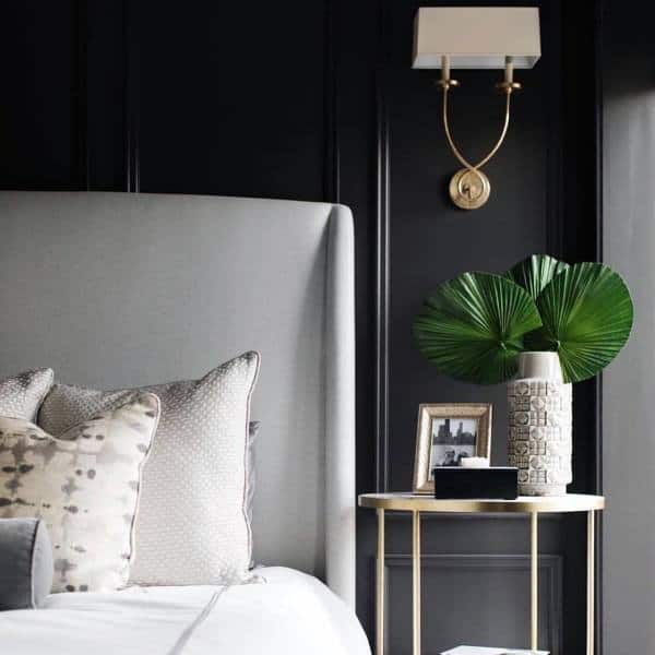 Sophisticated black bedroom with tufted headboard, gold wall sconce, and decorative accents.