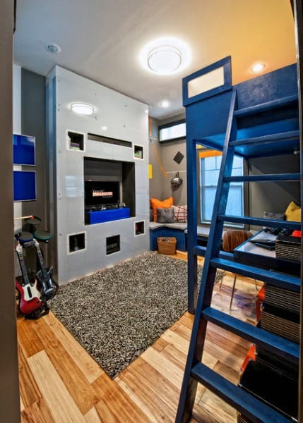 Small modern room with a loft bed, guitar, wall-mounted TV, and a rug on hardwood floor; cozy seating in the corner