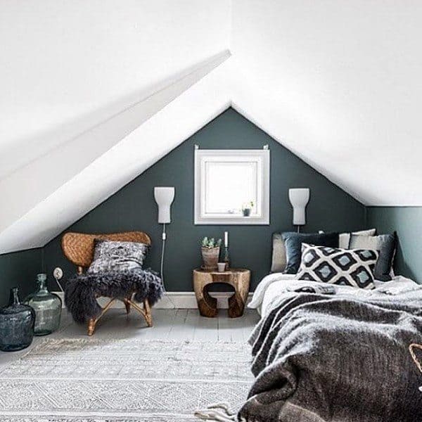 Cozy attic bedroom with a bed, patterned pillows, chair, and small window; dark green accent wall and soft lighting
