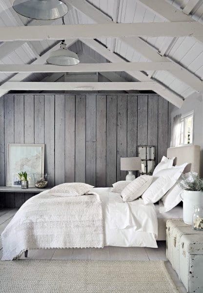 Cozy attic bedroom with white bedding, wood-paneled walls, and soft lighting under a pitched roof with exposed beams