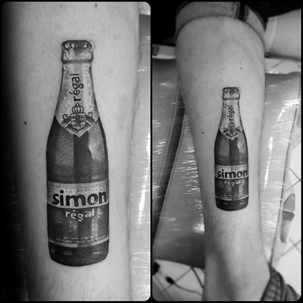 Realistic black and gray tattoo of a custom beer bottle labeled "Simon Regal," mimicking the design of a classic premium brew on the calf.