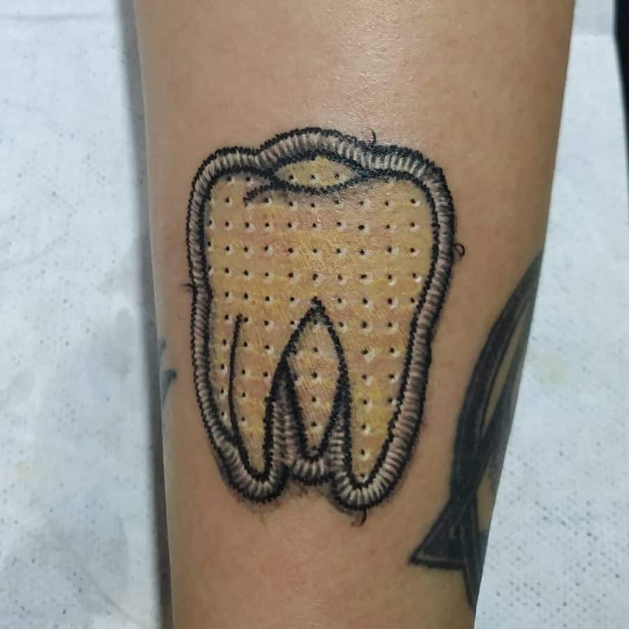 Patch-style embroidered tattoo of a tooth with a quilted texture and bold stitched border for a fabric illusion.