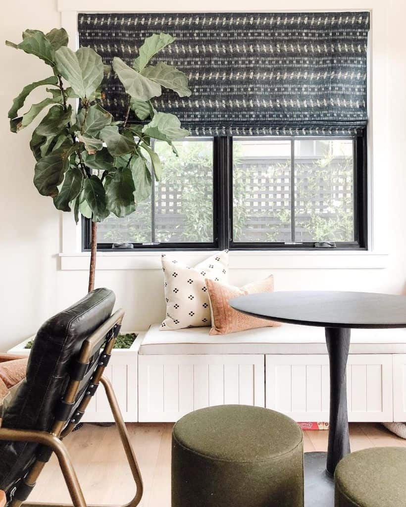 Bench seat banquette with patterned window shades, potted plant, and round table.