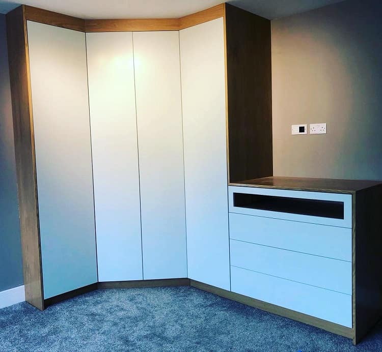 White corner bedroom closet with integrated drawers and wood accents.