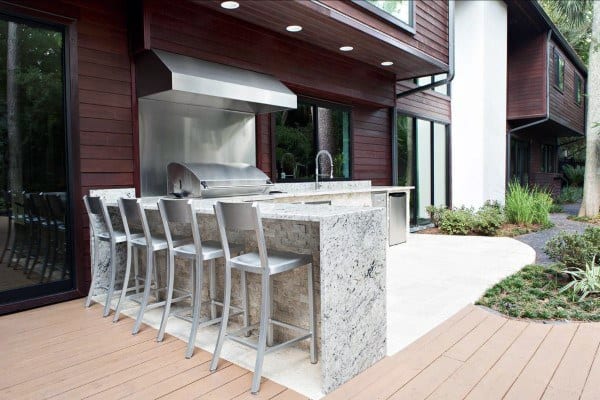 Outdoor kitchen with marble countertop, grill, stainless steel appliances, and bar seating.