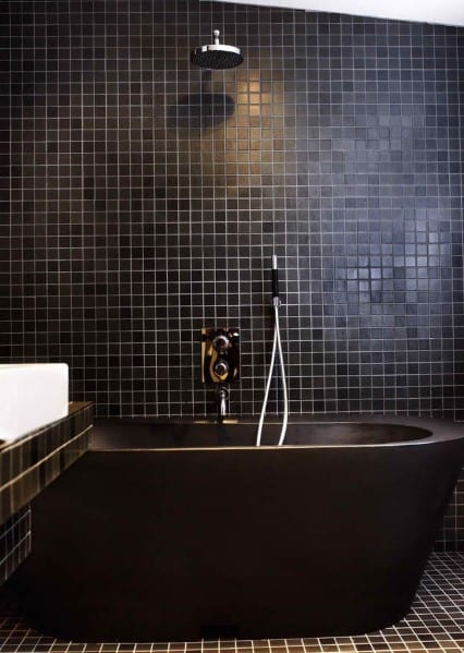 A modern bathroom with a black bathtub and black tiled walls and floor