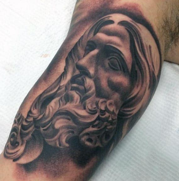 Black and grey tattoo of a bearded figure with flowing hair, resembling a classical sculpture, detailed with shading and depth