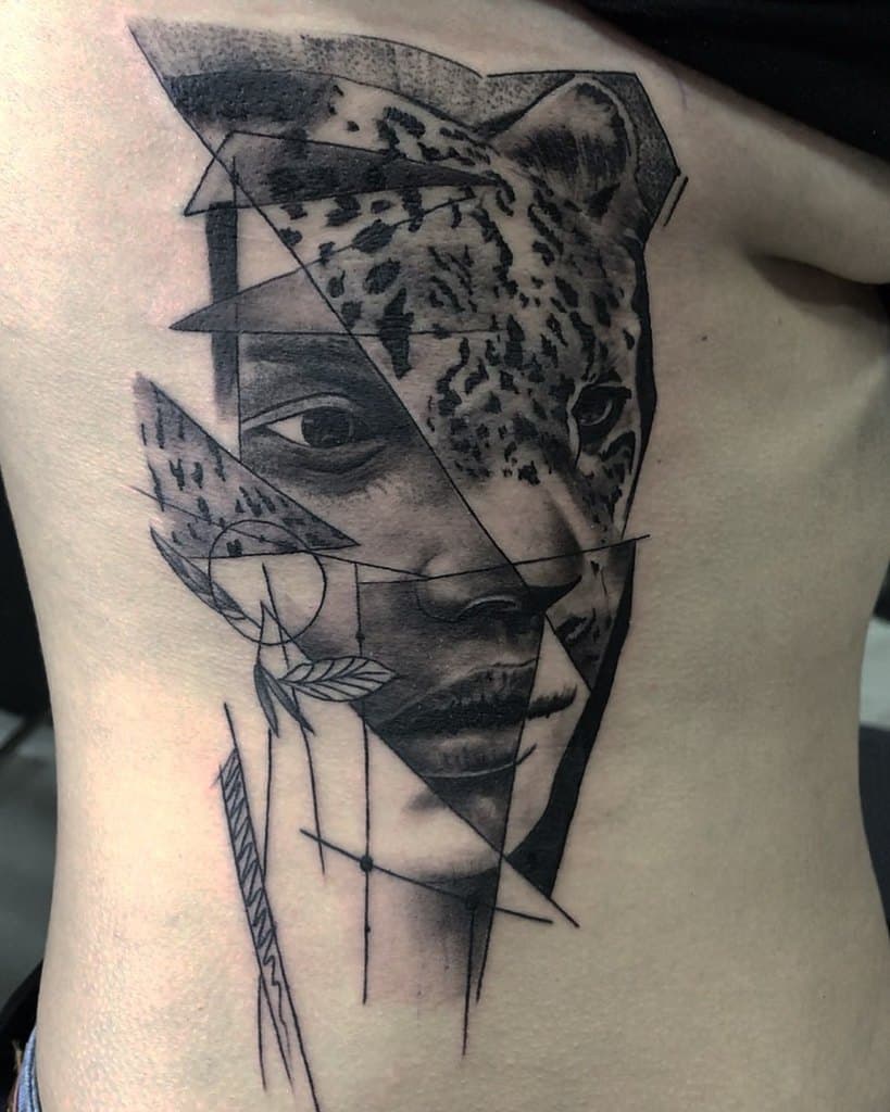 A striking geometric tattoo blending the face of a jaguar and a human, fragmented into angular pieces with fine detailing, placed on the side of the torso.