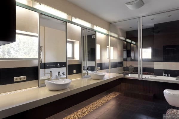 Modern bathroom with long countertop, twin sinks, large mirrors, and bathtub by the window