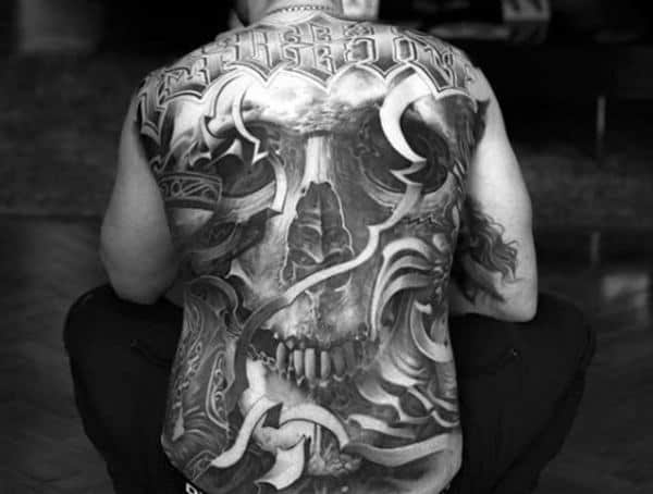 Full back tattoo for men featuring a detailed skull design with swirling abstract elements and bold lettering across the shoulders.