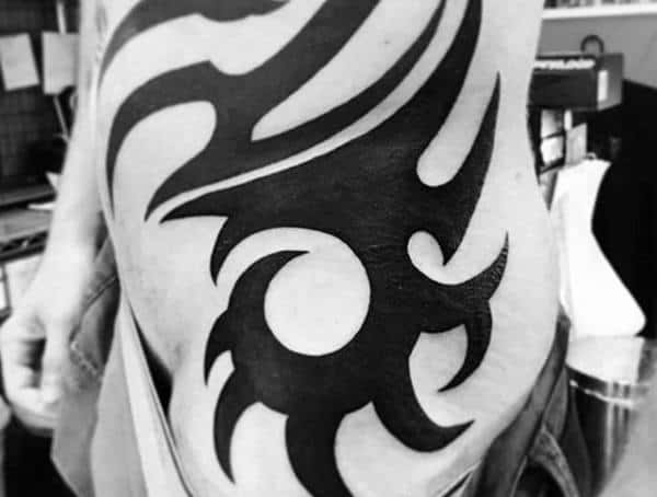 Side torso tattoo for men featuring a bold black tribal design with sharp curves and pointed edges.