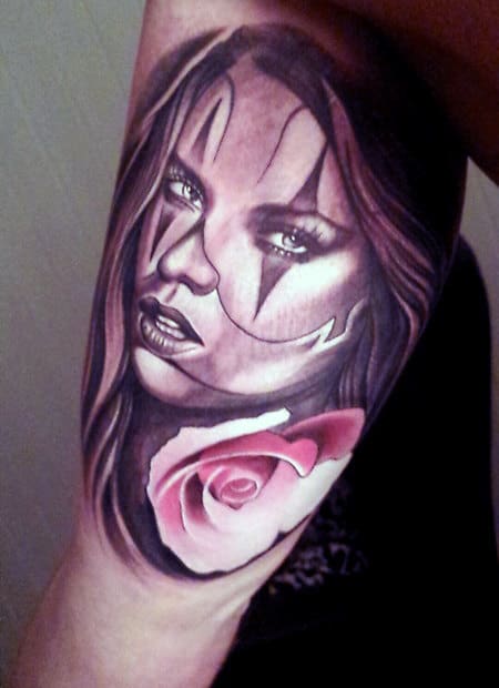 Tattoo of a woman's face with clown makeup and pink rose on a person's arm