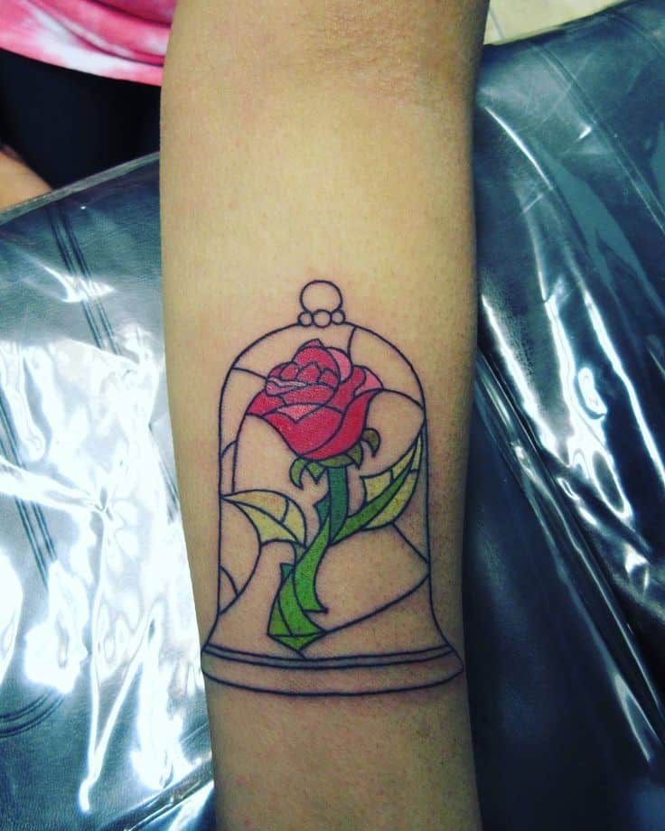Stained glass-style tattoo of the enchanted rose inside a glass dome, featuring bold outlines and vibrant red and green colors.