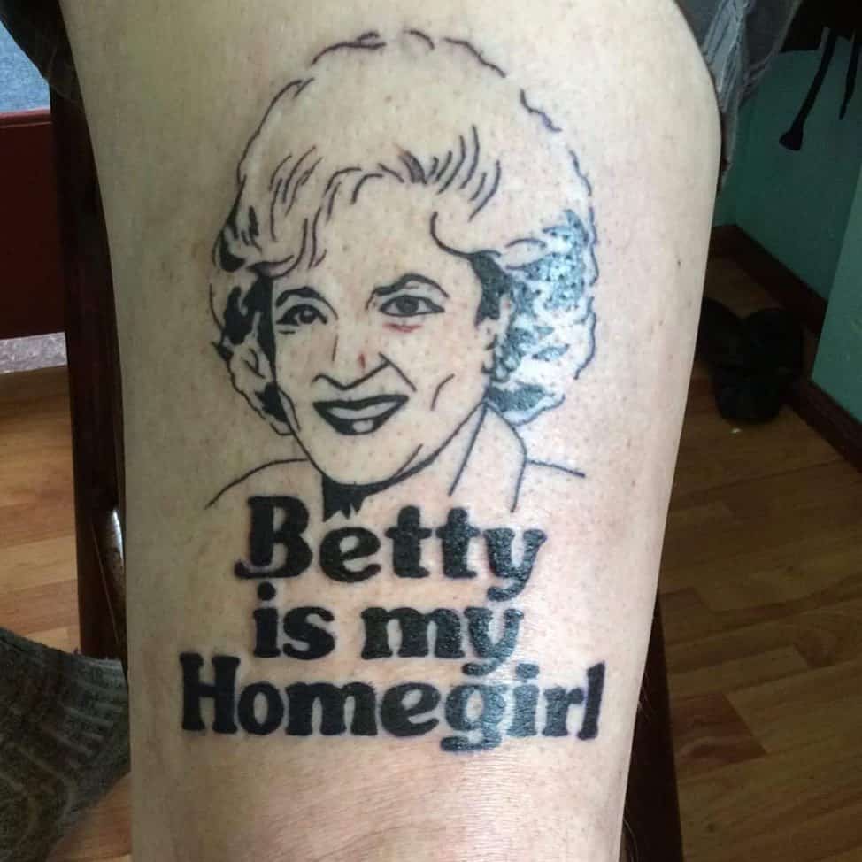 A black ink tattoo featuring a portrait of Betty White with the phrase 'Betty is my Homegirl' in bold lettering, placed on the thigh.