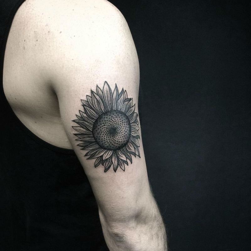 Black ink sunflower tattoo on upper arm with bold outlines, fine shading, and a detailed center for a striking and realistic floral design.
