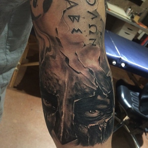 Arm tattoo of a gladiator's face with intense eyes in black and white design