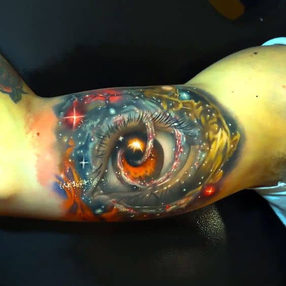 Tattoo of a cosmic eye blending with a swirling galaxy, featuring vibrant colors and intricate shading, inked on the upper arm.