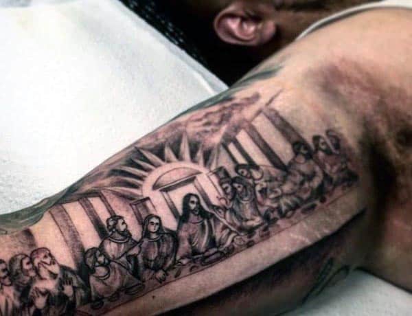 Black and grey tattoo of The Last Supper on the inner bicep, featuring Jesus and his disciples with architectural details and shading