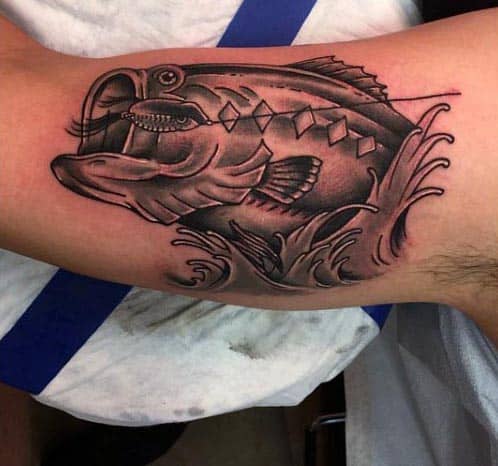 Black and grey tattoo of a largemouth bass jumping out of water with a fishing lure in its mouth, featuring bold lines and shading