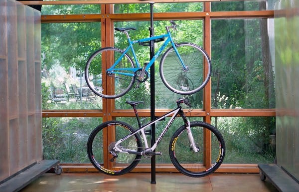 Two bikes mounted on a vertical floor-to-ceiling pole in a bright room with large windows.
