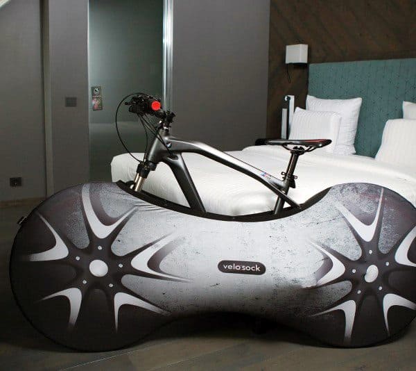Bicycle with a stylish protective cover placed inside a modern bedroom near a bed.