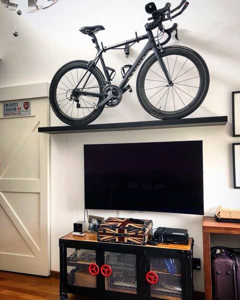 Black bicycle displayed on a floating shelf above a TV in a modern living room.