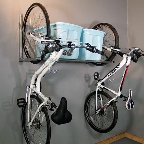 Garage with two bikes hanging on wall-mounted hooks and storage bins placed on a shelf above.
