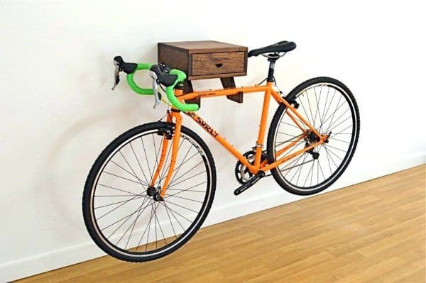 Garage with an orange bike mounted on a wooden wall rack featuring a small storage drawer.