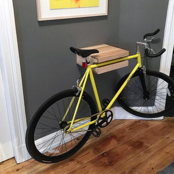 Yellow bike mounted on a minimalist wooden wall rack in a corner of a garage or room.
