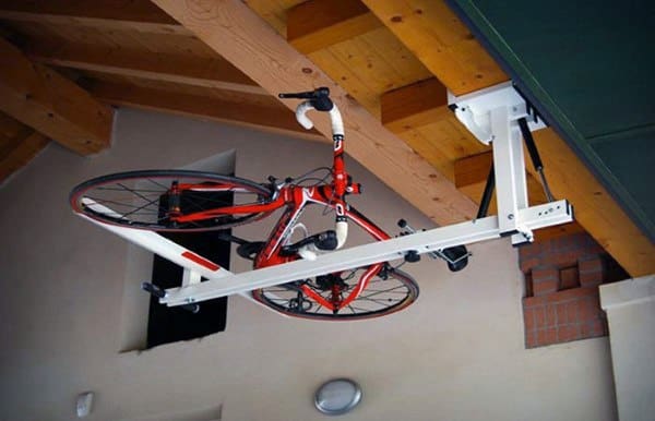 Red bicycle stored on a ceiling-mounted lift rack under wooden beams in a garage.