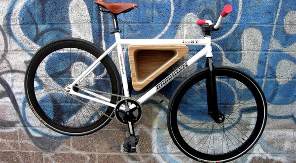 White bike mounted on a triangular wooden wall rack against a graffiti-covered wall.
