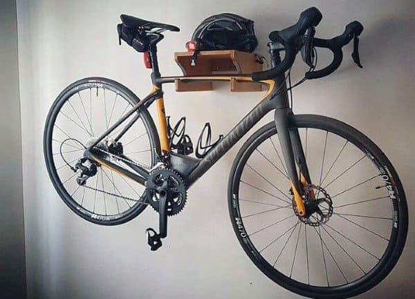 Garage with a black and yellow bike mounted on a wooden wall rack with a helmet on top.